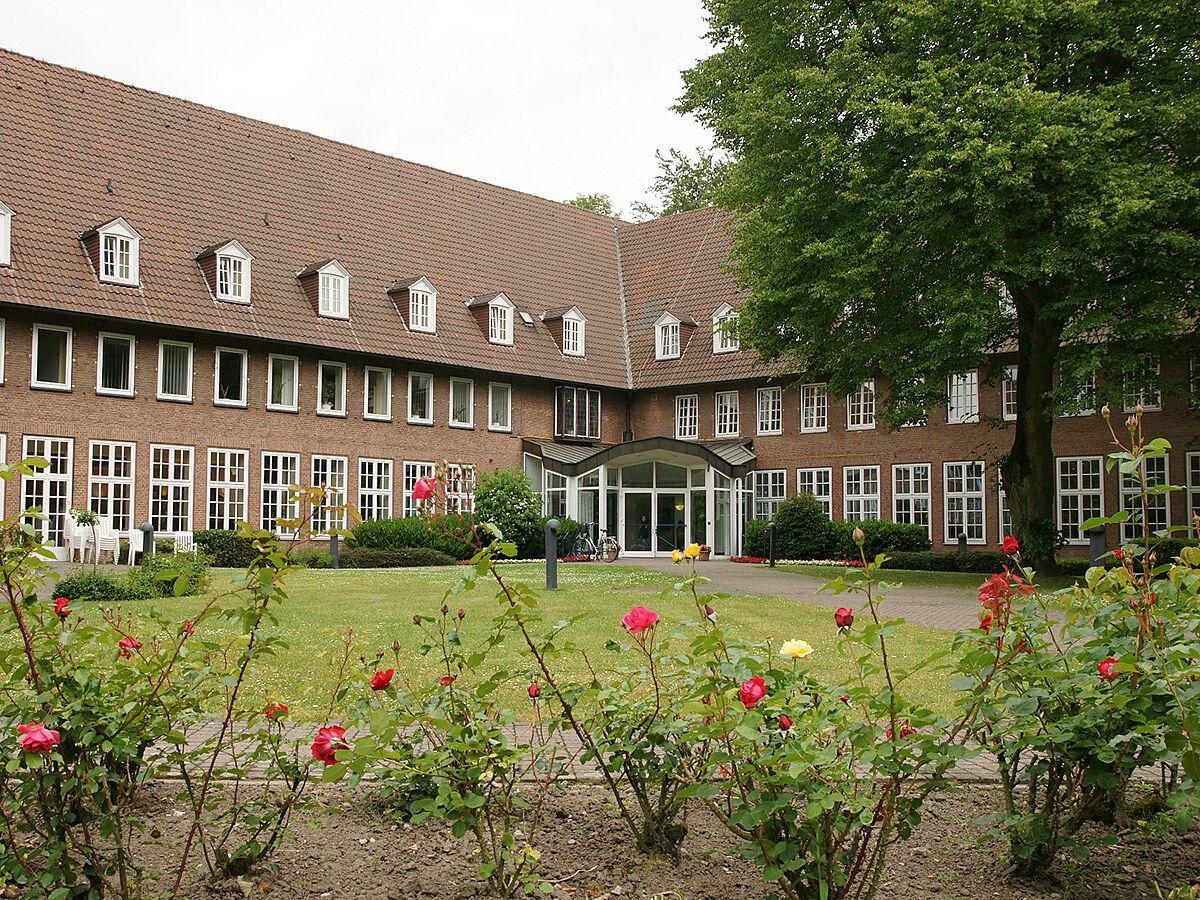 Haupteingang der Kolping-Bildungsstätte in Coesfeld, davor eine grüne Wiese, Blumen und ein Baum.