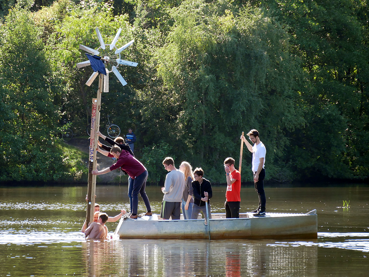 Jugendliche stellen von einem Boot aus ein Windrad in einem See auf.